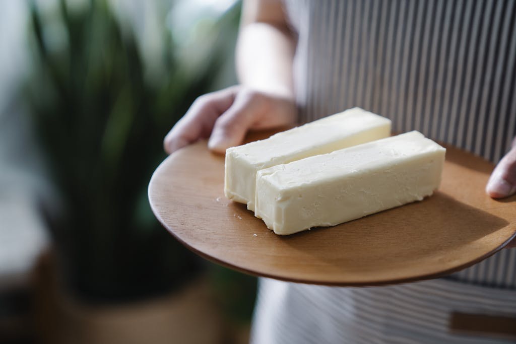 Close-up of hands holding a wooden plate with two sticks of butter.