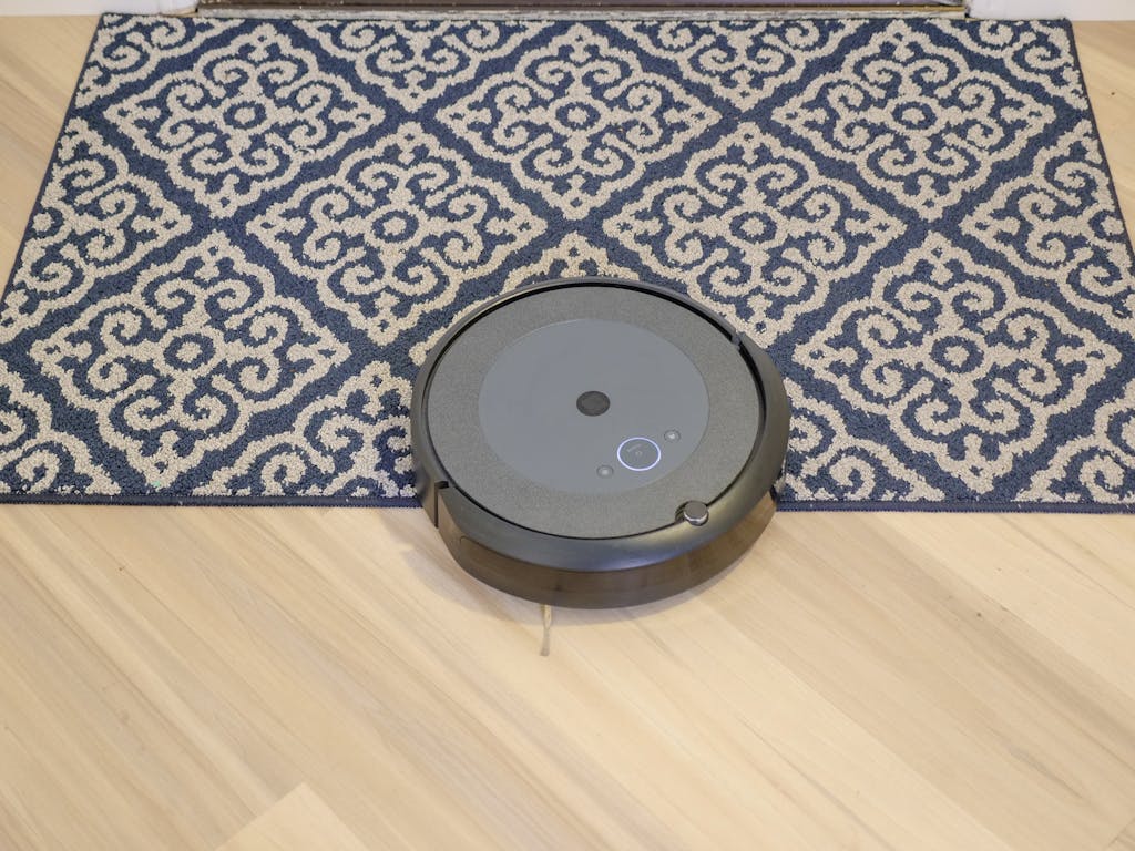 A modern robotic vacuum cleaning a stylish patterned carpet on a wooden floor.