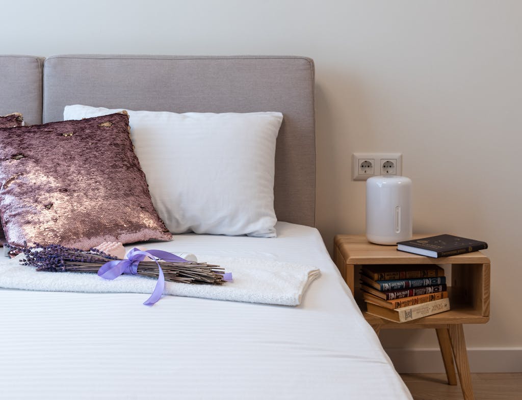 A serene bedroom setup featuring elegant pillows, fresh lavender, and a modern side table with books.