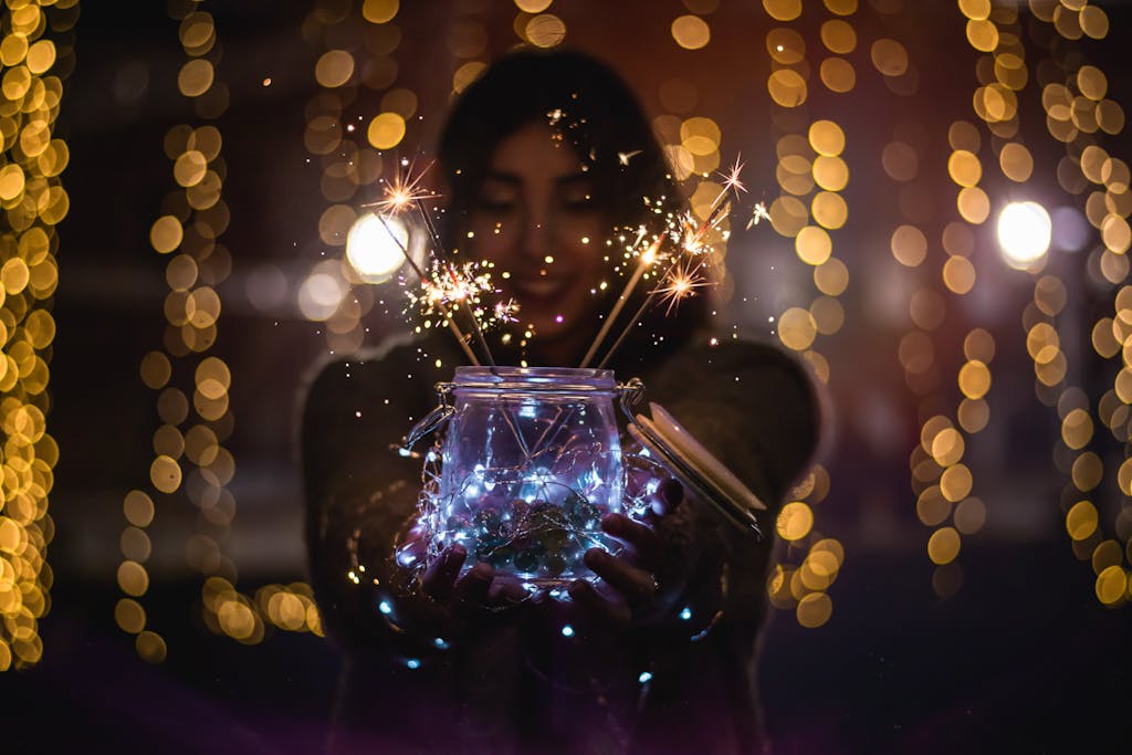 A woman holds a jar of sparklers, surrounded by glowing bokeh lights, capturing a magical night scene.