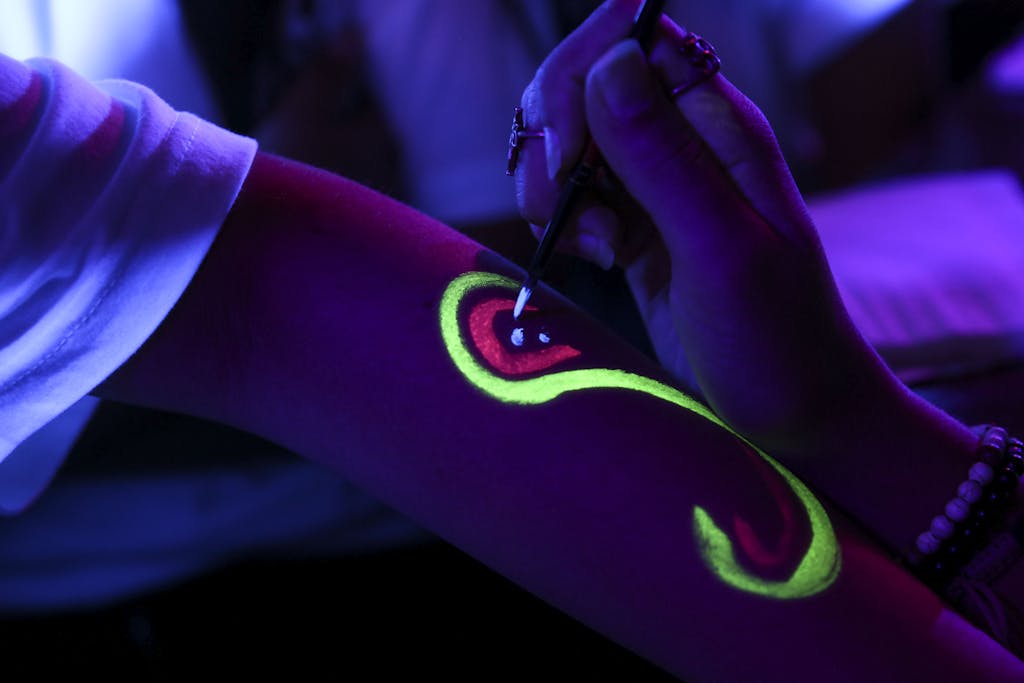 Close-up of fluorescent body paint being applied under blacklight.