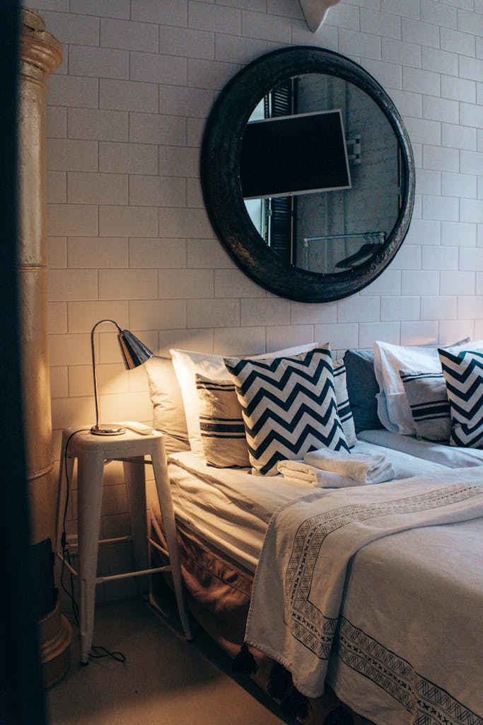 Elegant bedroom with cozy pillows, stylish lamp, and mirror accent showcasing modern interior design.