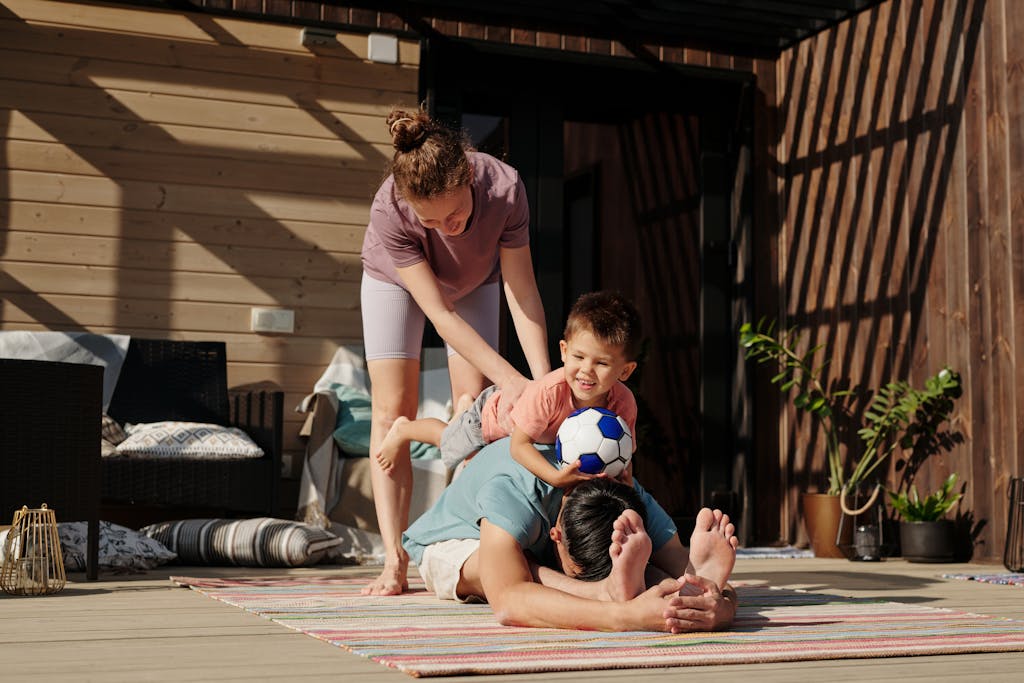Family engaging in playful yoga on a sunlit porch, bonding and exercising together.