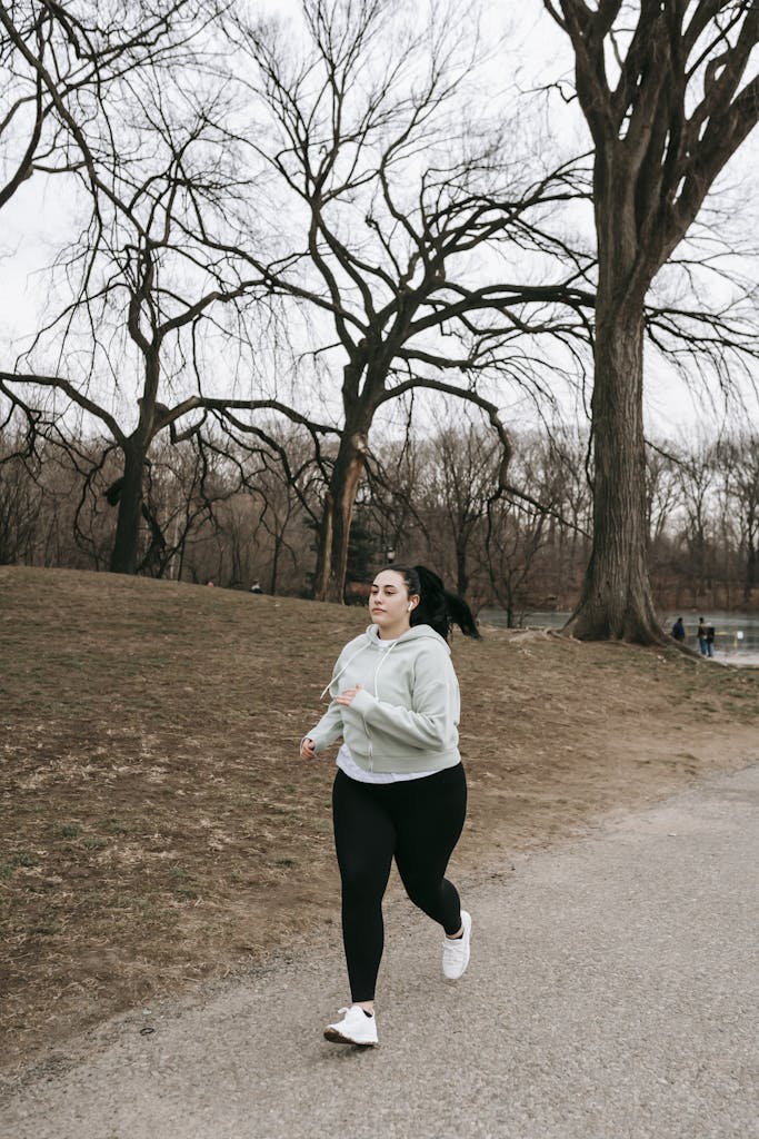 Full body motivated plus sized female in gray hoodie running in autumn park