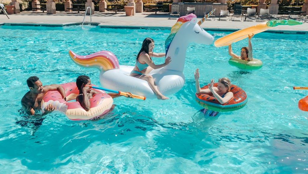 Group of adults enjoying a summer pool party with colorful inflatable floats and water guns.