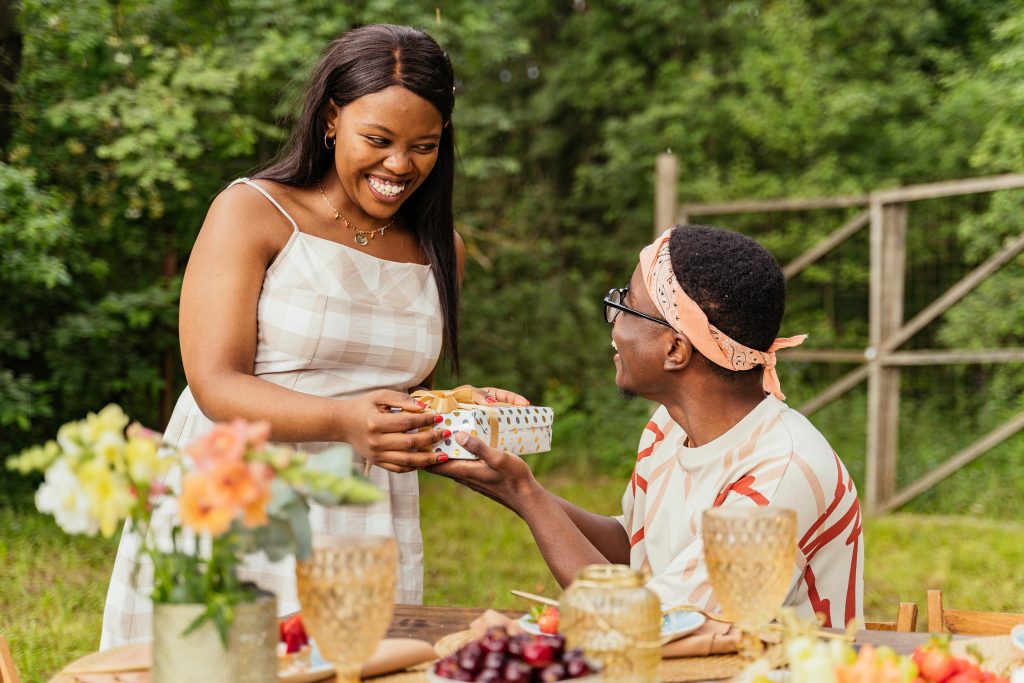 A joyful moment of gift exchange between friends at an outdoor summer gathering.