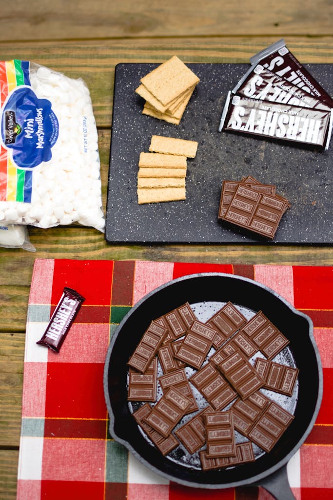 Preparing s'mores outdoors with chocolate, graham crackers, and marshmallows.