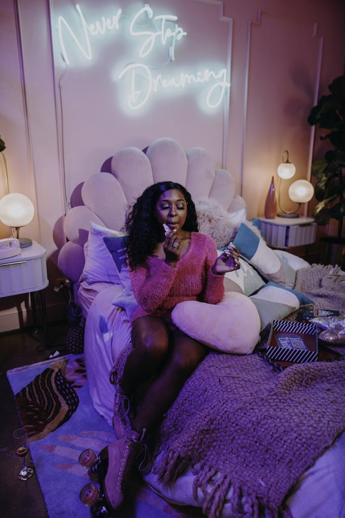 Teen girl in a cozy, stylish bedroom with neon 'Never Stop Dreaming' sign.