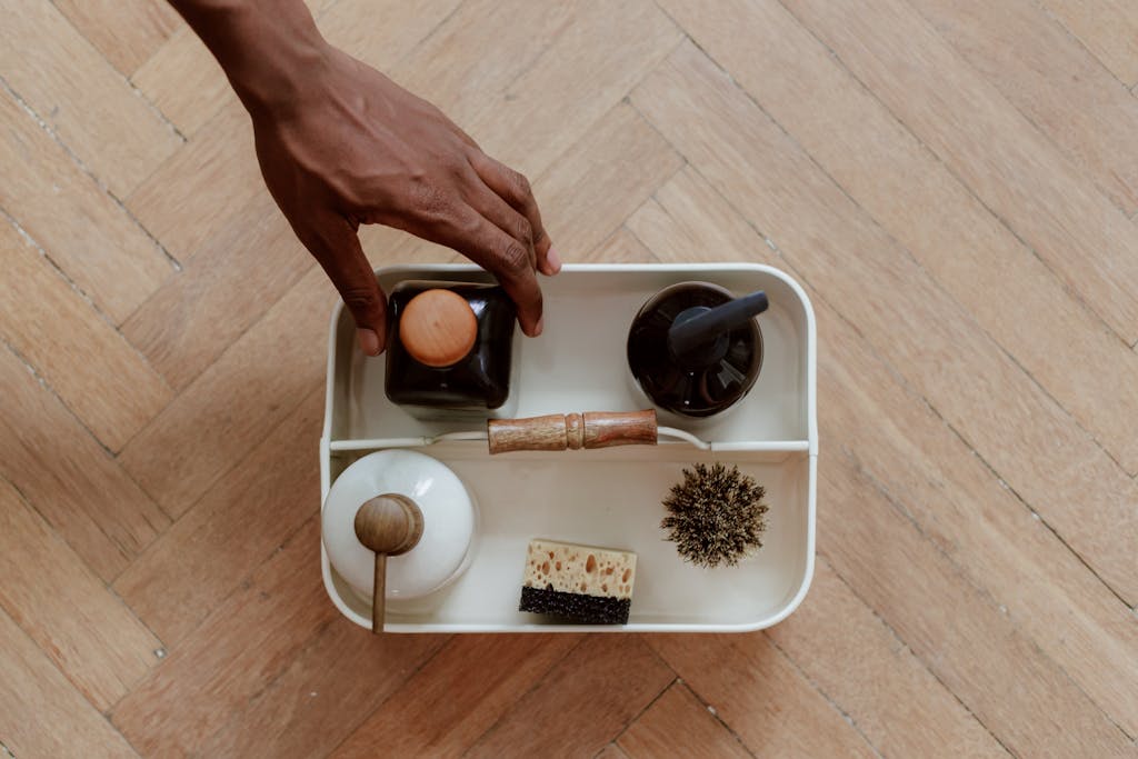 Top view of a cleaning kit with brush, sponge, and bottles on a wooden floor.