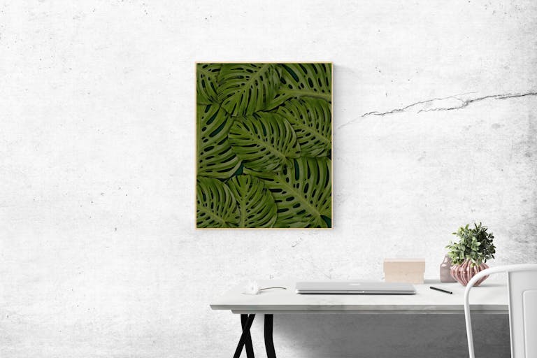 A stylish minimalist office setting featuring a framed green leaf artwork and sleek white desk.