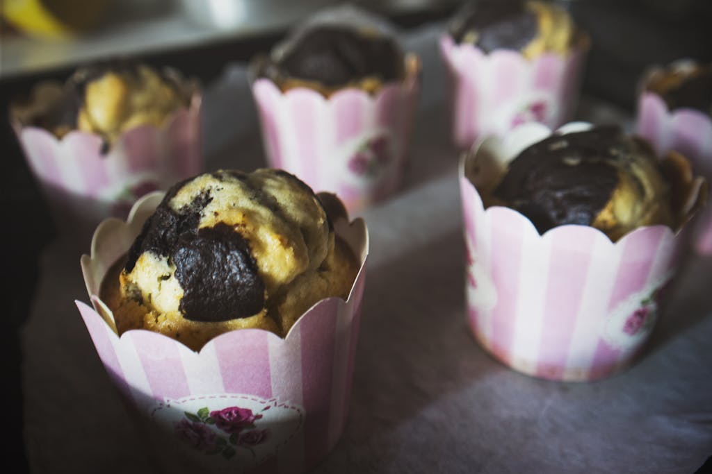 Close-up of homemade muffins with chocolate swirl in pink floral liners, perfect for dessert lovers.