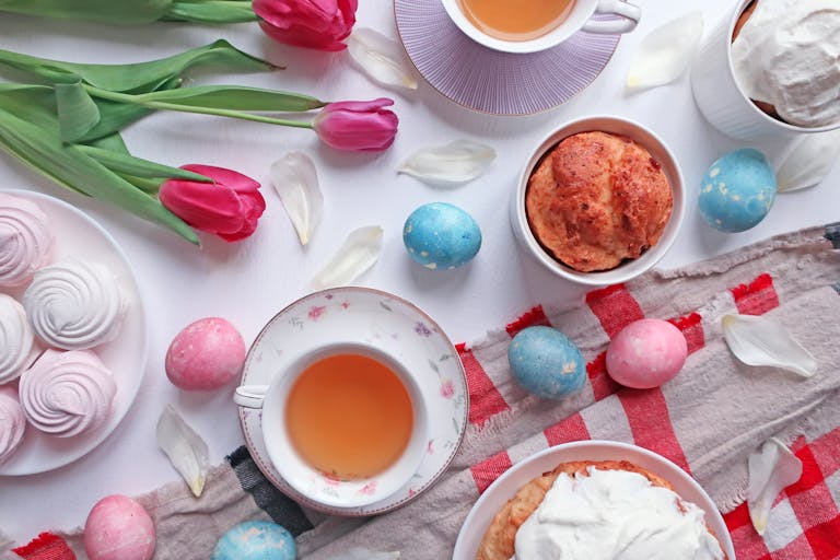 Colorful Easter tea party setup with tulips, pastries, and decorated eggs on a white table.