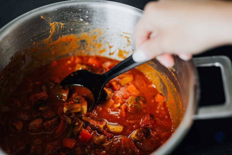 Freshly cooked vegetable stew with tomatoes and spices in a pot, stirred by hand.