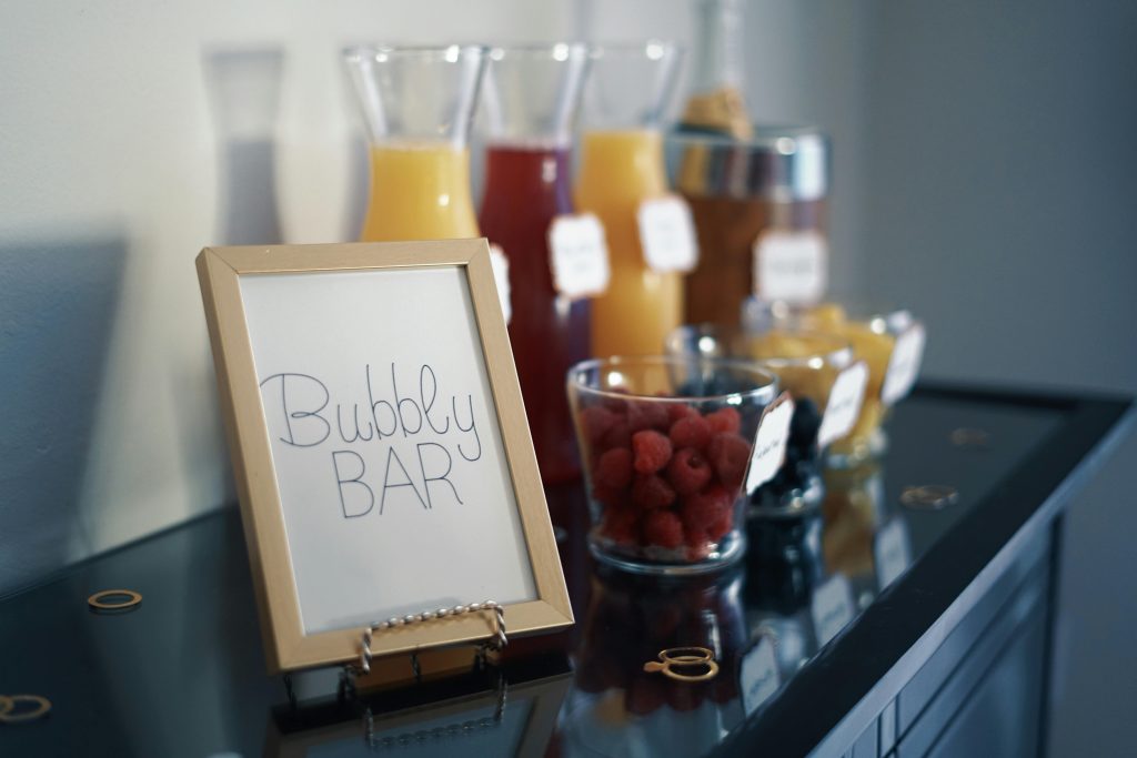 A sophisticated bubbly bar arrangement featuring juices, fresh raspberries, and an inviting sign.