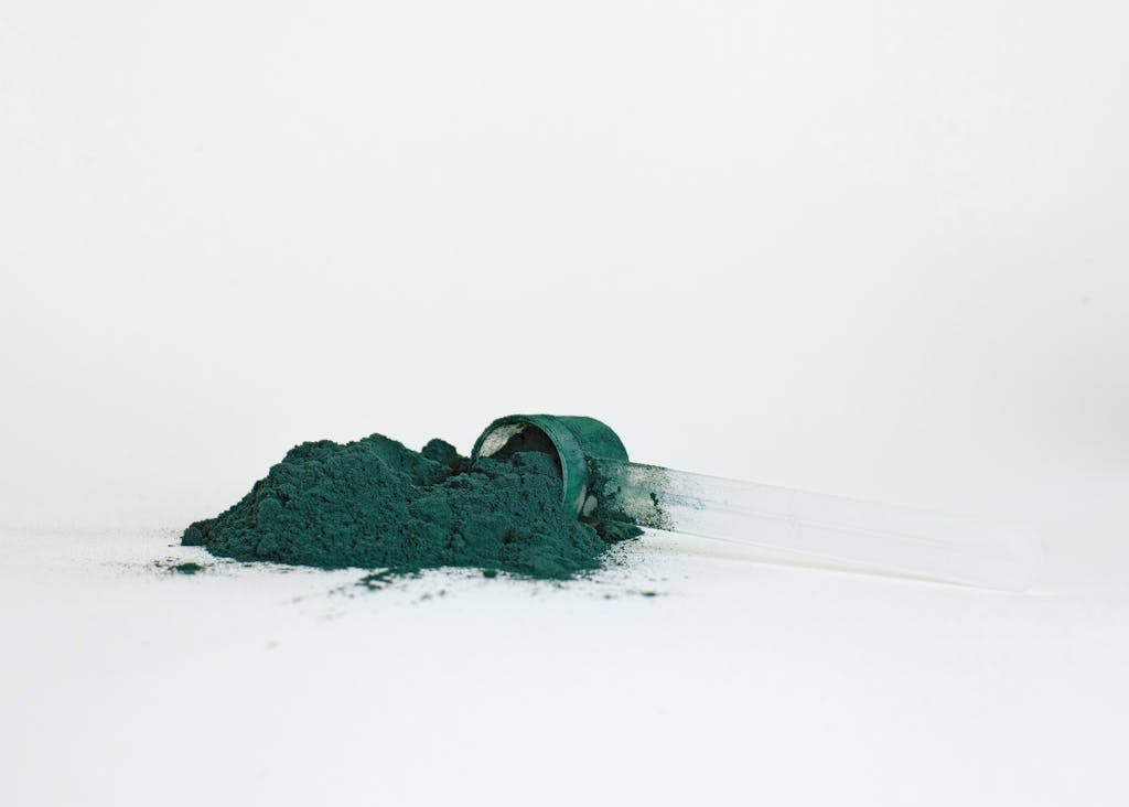 A pile of spirulina powder in a transparent measuring scoop isolated on a white background.
