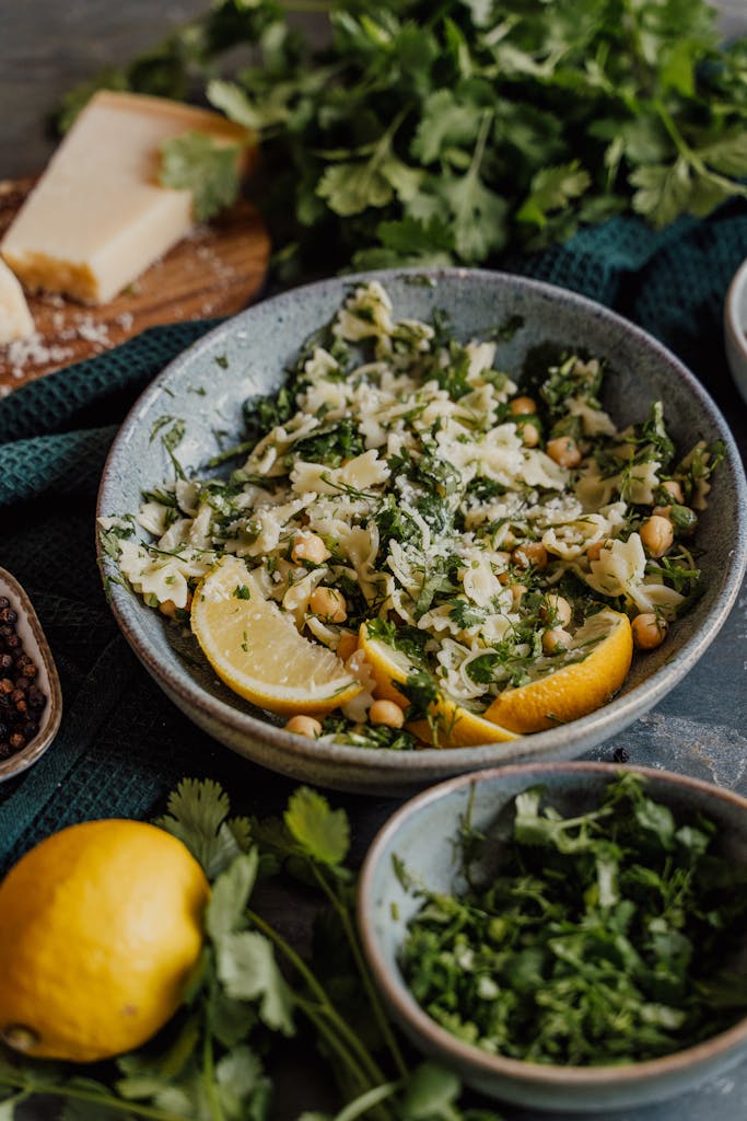 Bowl of delicious herb-infused pasta salad with lemon slices and chickpeas on a rustic table.