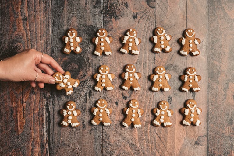 A hand reaching for a gingerbread man among a batch of festive cookies on a wooden surface.