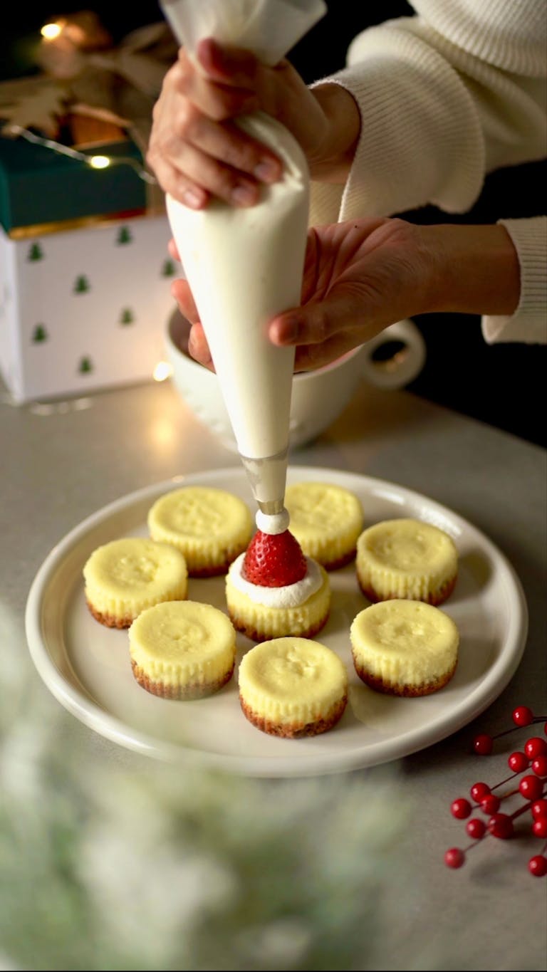 Hands decorating mini cupcakes with strawberries and cream frosting. Perfect for holiday celebrations.