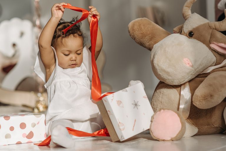 Cute child unwrapping gifts with a plush toy, showcasing joy and innocence indoors.