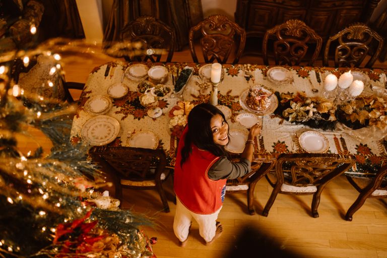 A woman preparing a beautifully decorated Christmas dinner table with festive lights.