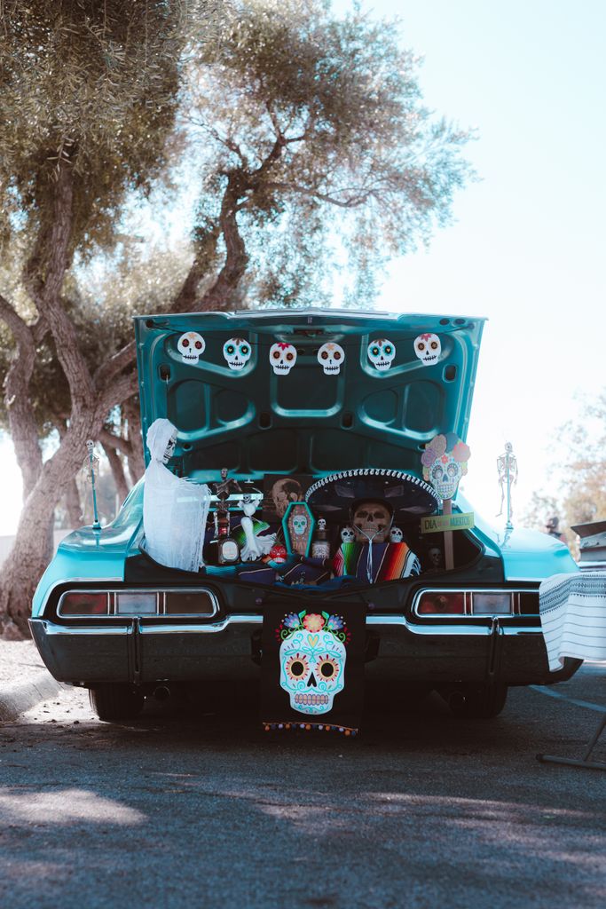 Classic car trunk filled with vibrant Halloween decorations featuring skulls and spooky ornaments.