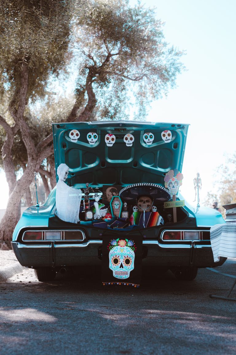 Classic car trunk filled with vibrant Halloween decorations featuring skulls and spooky ornaments.