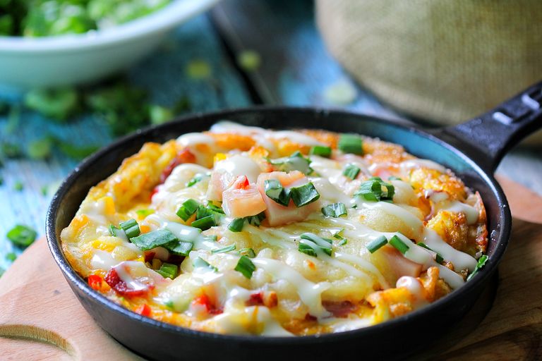 Close-up of a cheesy skillet dish topped with fresh herbs and green onions, perfect for food lovers.