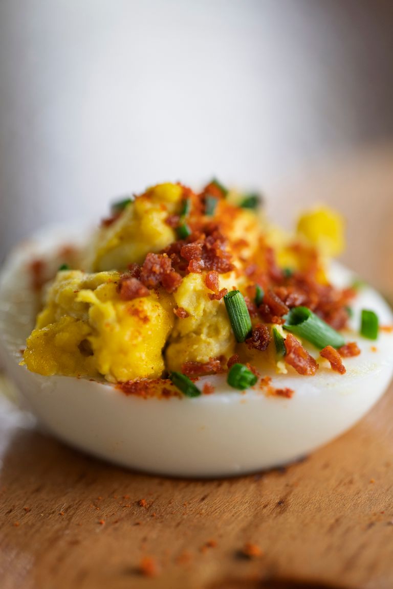 Close-up of a deviled egg topped with crispy bacon and chives.
