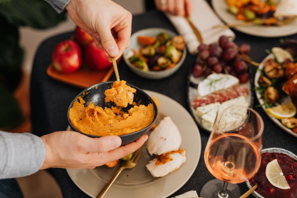 Close-up of hands serving mashed potatoes from a bowl at a festive dinner table.