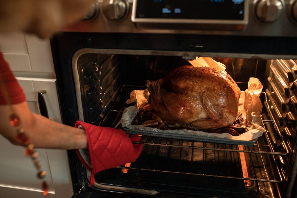 Golden roasted turkey being taken out of the oven, perfect for Thanksgiving dinner imagery.