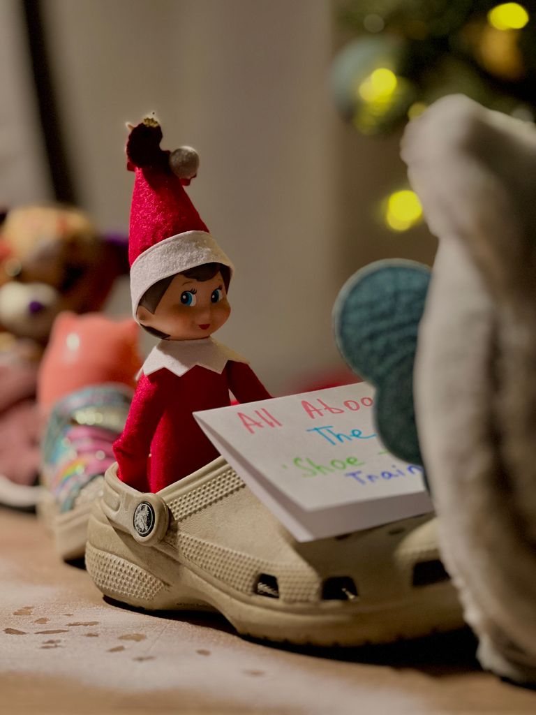 Whimsical elf figure in red hat rides a shoe train with festive background.